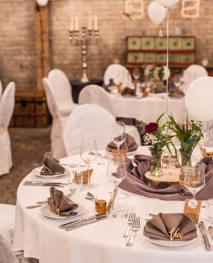 Stühle und Tische in Weiß verkleidet, Dekoration mit Blumen, Luftballons und Tischnamen aus Holz